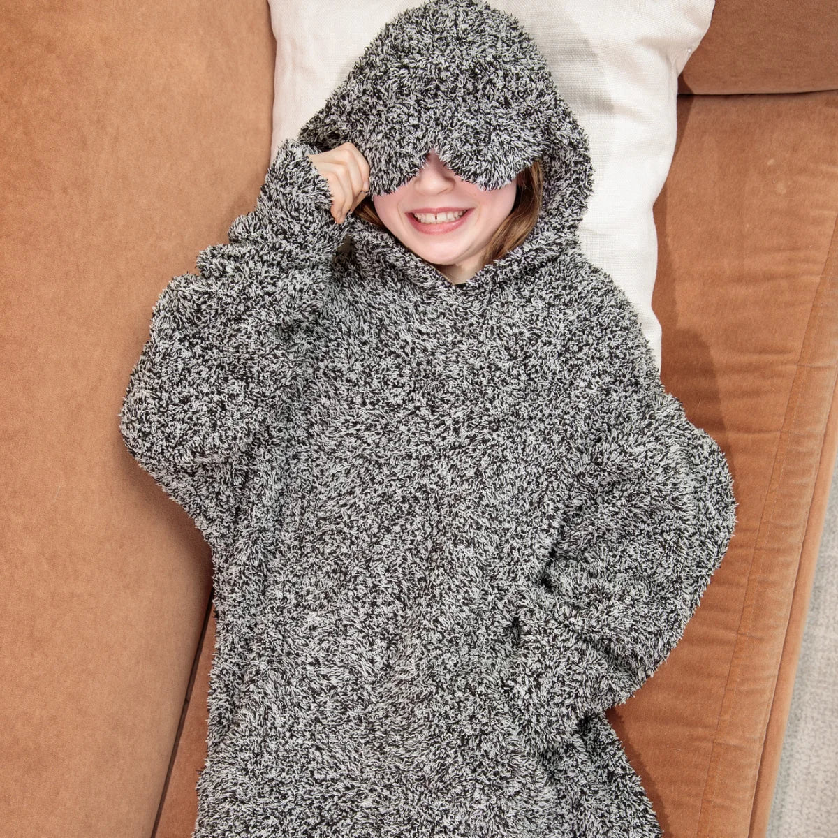Man wrapped in charcoal heathered oversized hoodie blanket on white bedding, overhead view