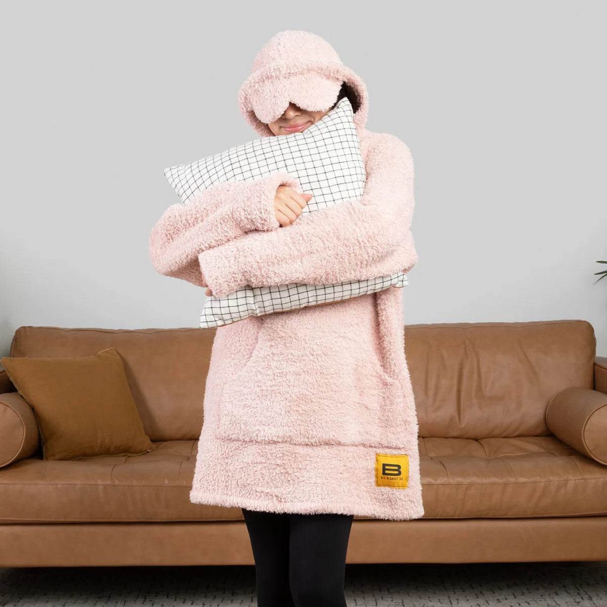 Person wrapped in pink oversized hoodie blanket with hood up, holding tablet on bed