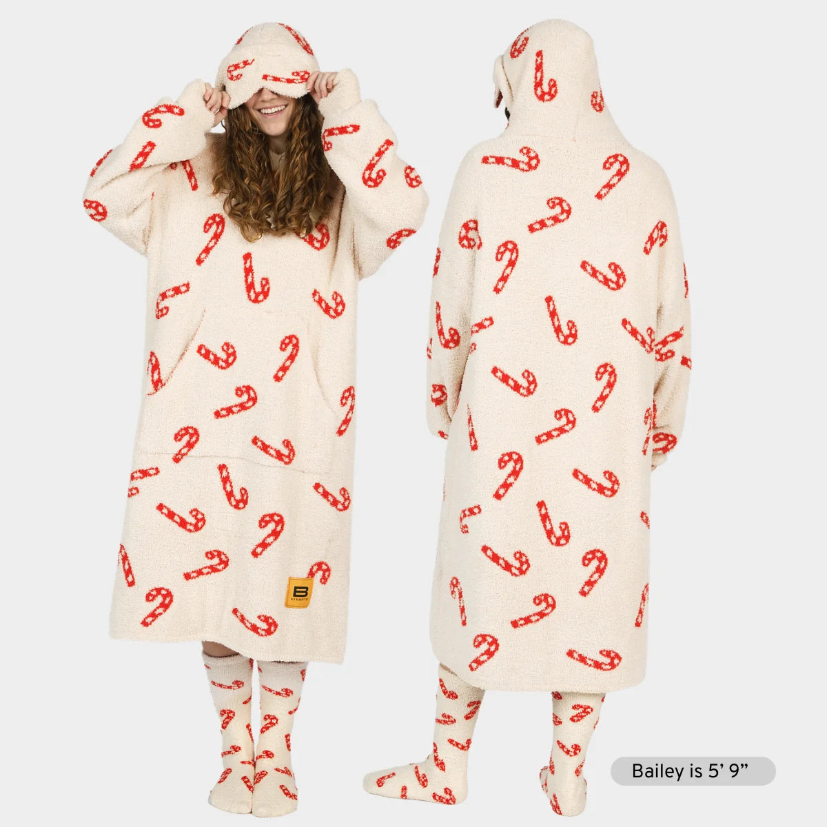 Cream oversized hoodie blanket with red candy cane pattern, modeled front and back with matching socks and hood pulled over eyes