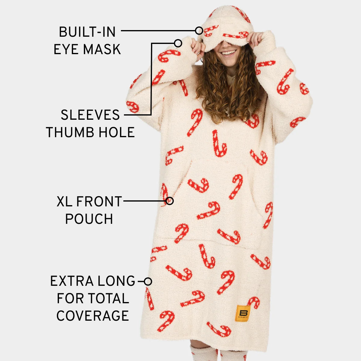 Cream oversized hoodie blanket with red candy cane pattern, featuring built-in eye mask, thumb hole sleeves, XL front pouch, and extra-long coverage
