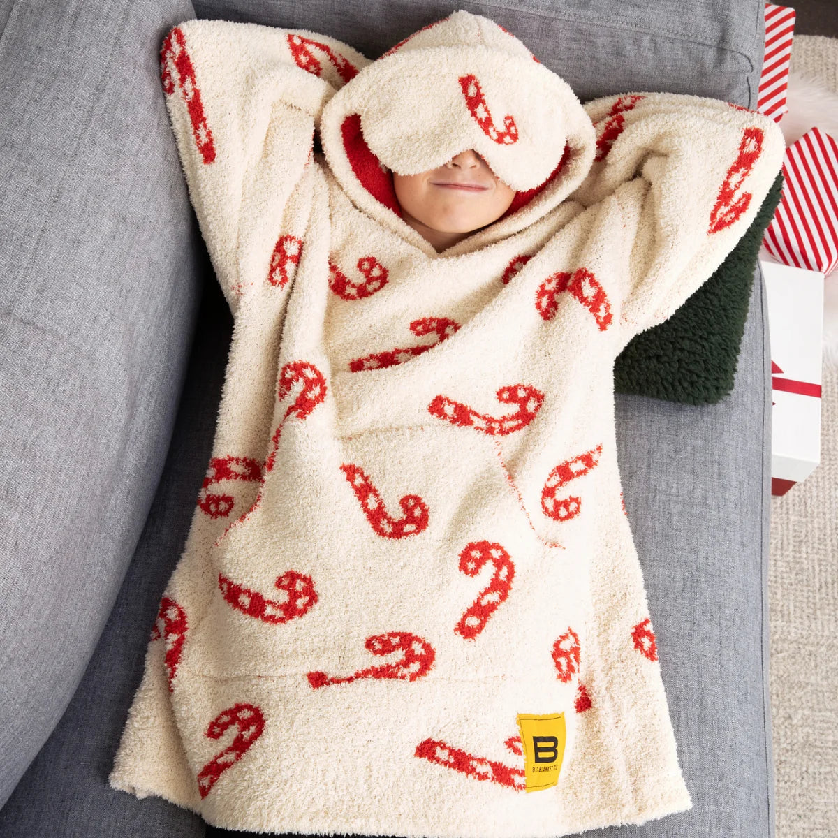 Child wrapped in cream oversized hoodie blanket with red candy cane pattern