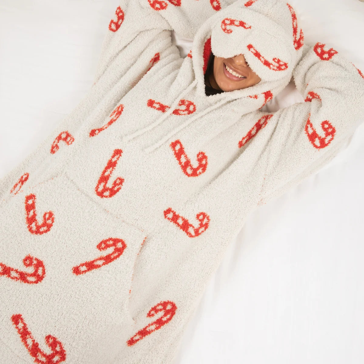 Person wrapped in cream oversized blanket hoodie with red candy cane pattern, smiling from under hood