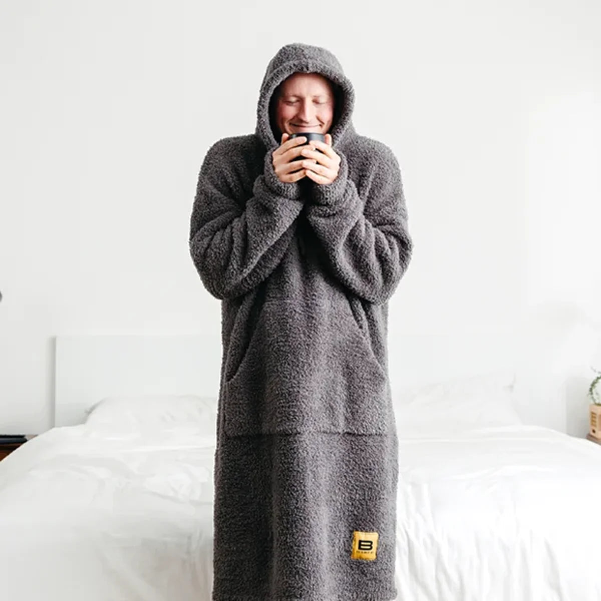Person wearing charcoal Premier Plush™ Hoodie blanket with hood up, standing on bed, cozy and warm