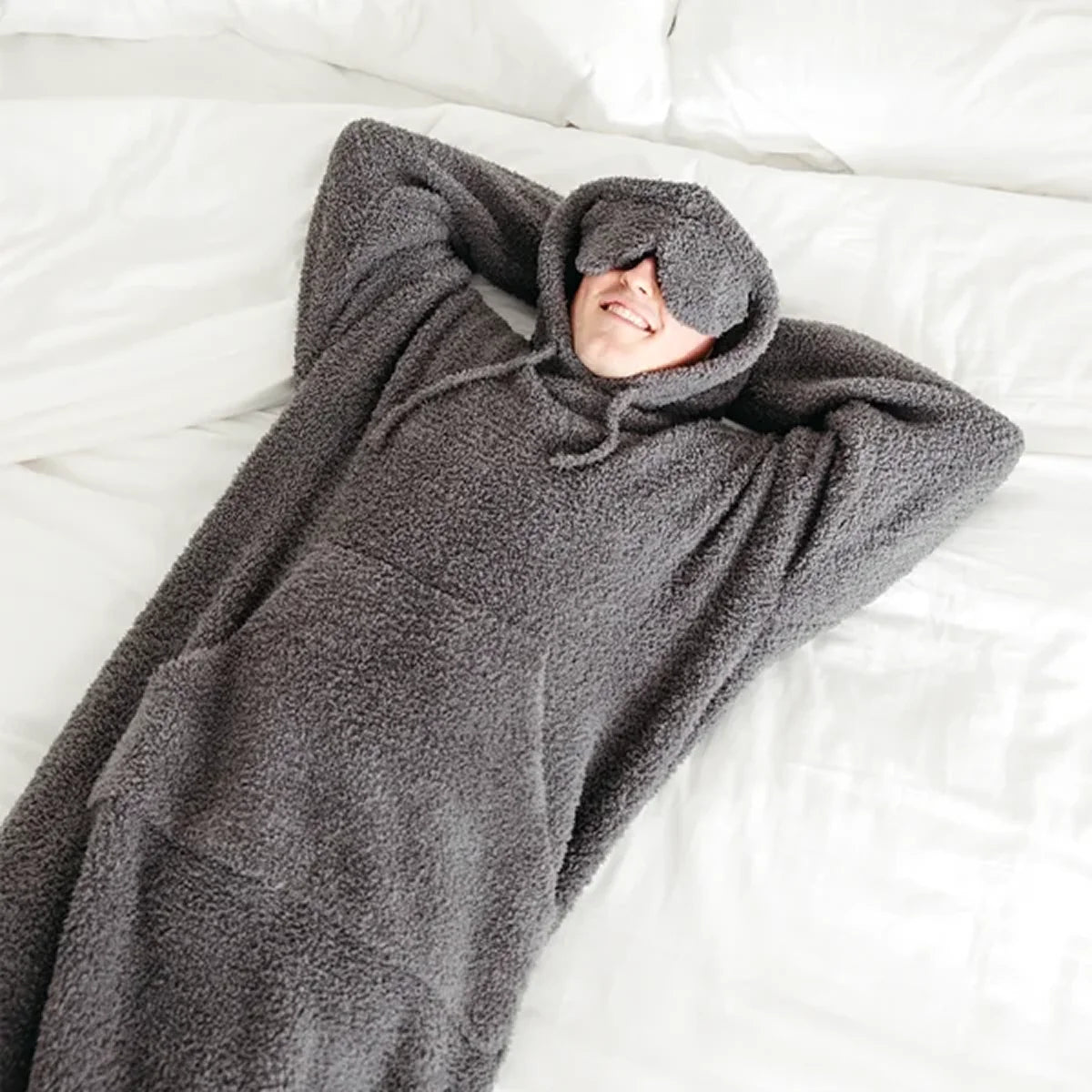 Child wrapped in charcoal gray oversized hoodie blanket on white bedding, smiling with head covered