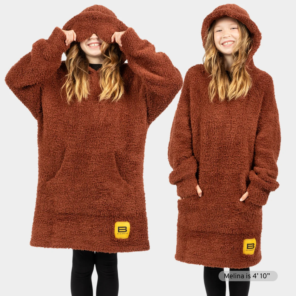 Chocolate brown oversized plush hoodie blanket with hood and front pocket, shown on two models wearing it as a wearable blanket