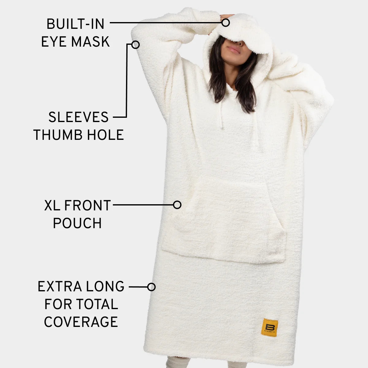 Woman wearing cream oversized hoodie blanket with built-in eye mask, thumb hole sleeves, and XL front pouch
