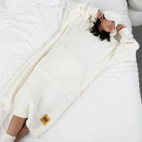 Person wrapped in cream Premier Plush™ Hoodie blanket on bed, showing cozy oversized fit and soft texture