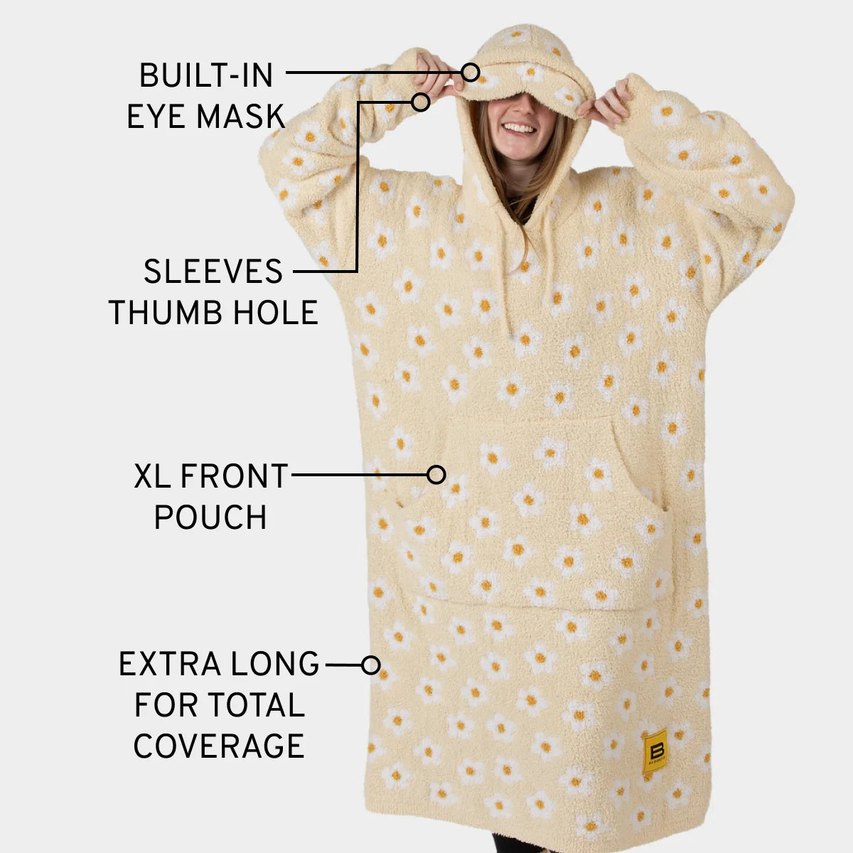Cream oversized blanket hoodie with yellow daisy pattern, featuring built-in eye mask, thumb holes, XL front pouch, and extra-long length
