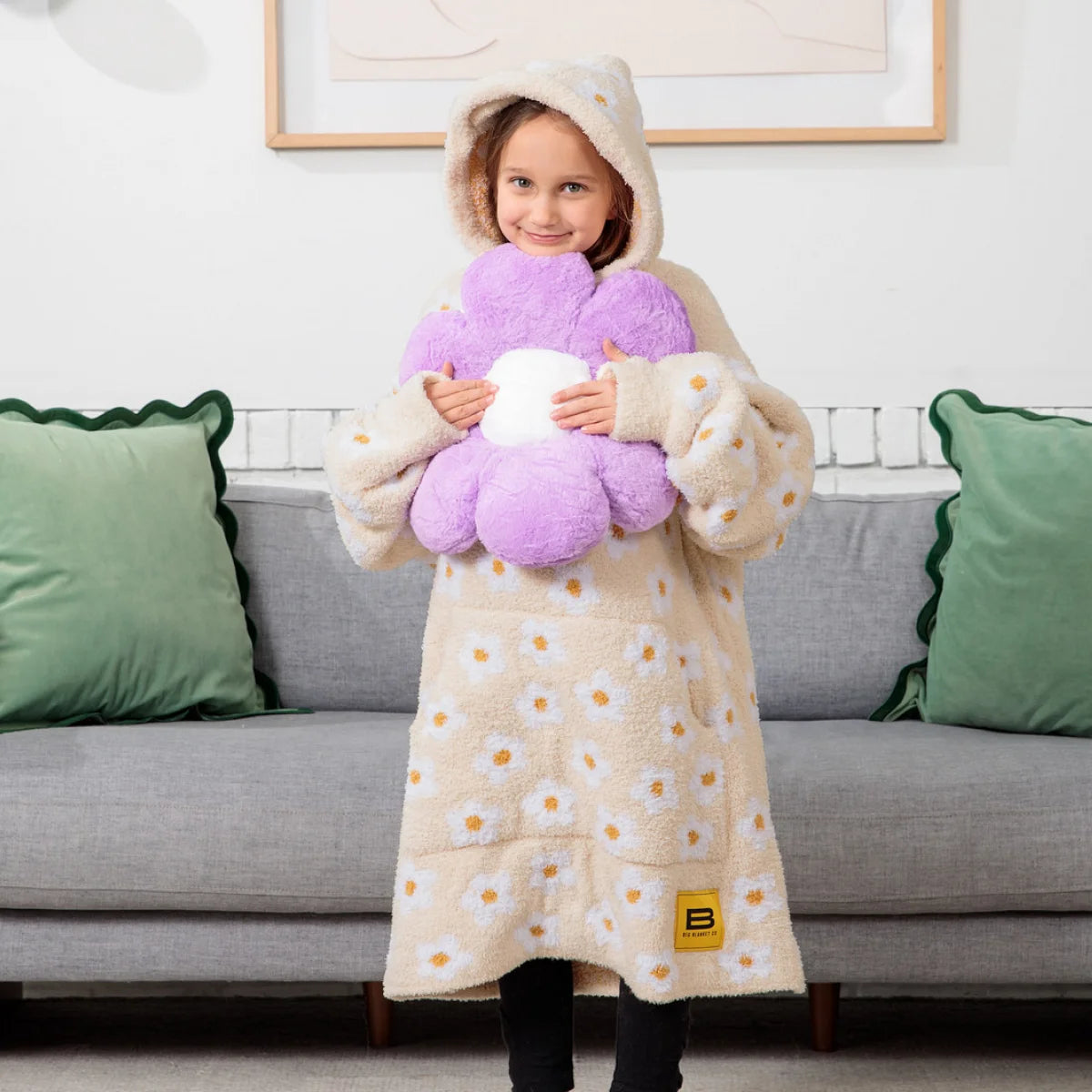Cream oversized hoodie blanket with yellow and white daisy pattern, modeled by smiling woman wearing hood up