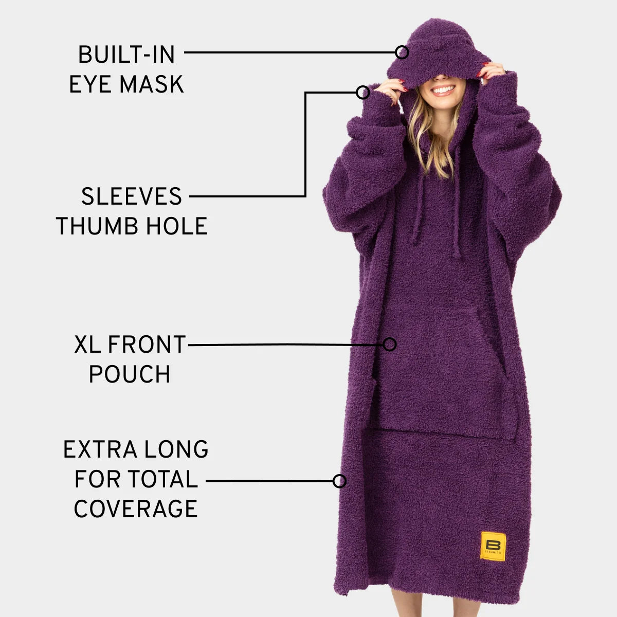 Woman wearing deep purple oversized hoodie blanket with built-in eye mask, thumb hole sleeves, and front pouch