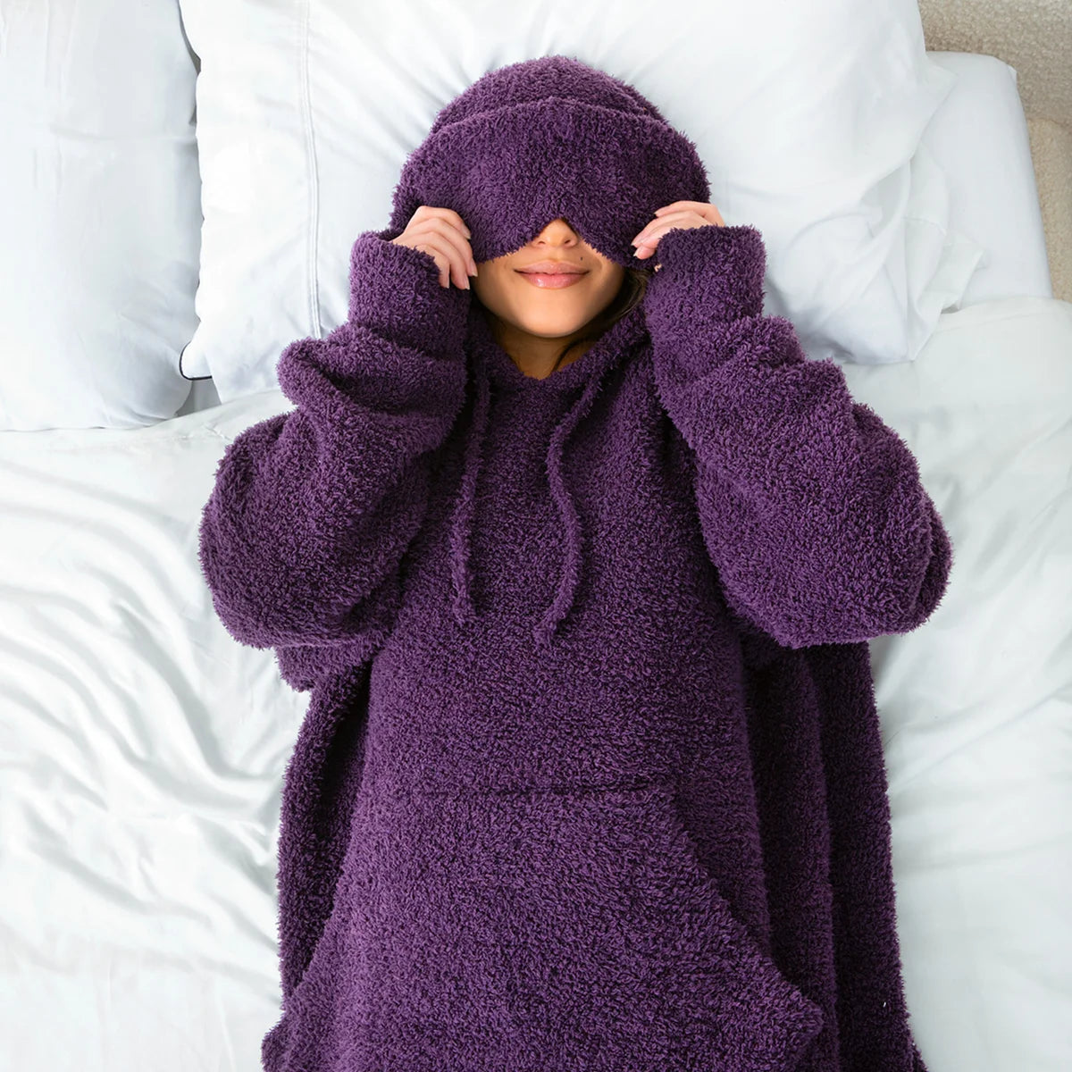 Child wrapped in deep purple oversized hoodie blanket on white bedding, pulling hood over face
