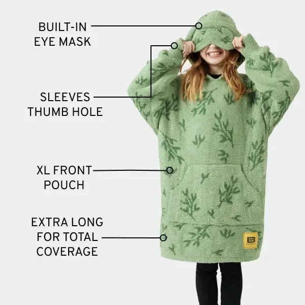 Oversized green hoodie blanket with fern print, built-in eye mask, thumb hole sleeves, and front pouch, modeled by child