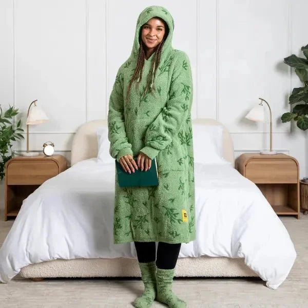 Woman wearing oversized green textured hoodie blanket with white pillows and bedding in modern bedroom