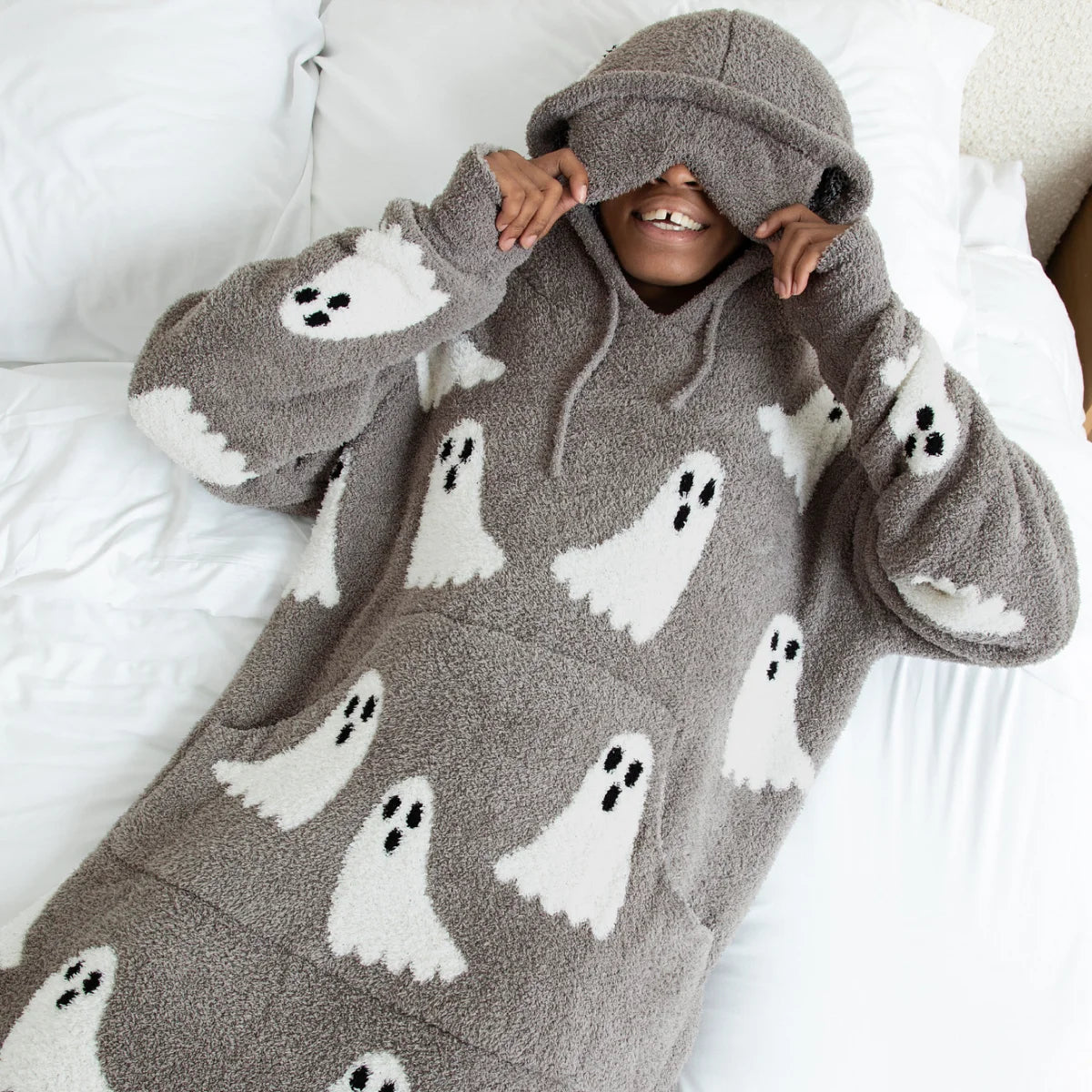 Person wrapped in gray oversized blanket hoodie with white ghost and black eyes pattern design