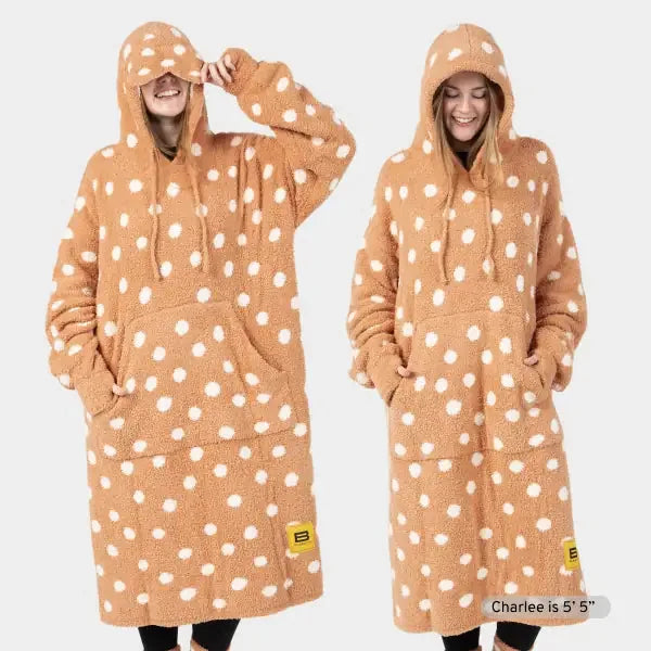 Tan oversized hoodie blanket with white polka dots, front pocket, and drawstring hood, shown on two models