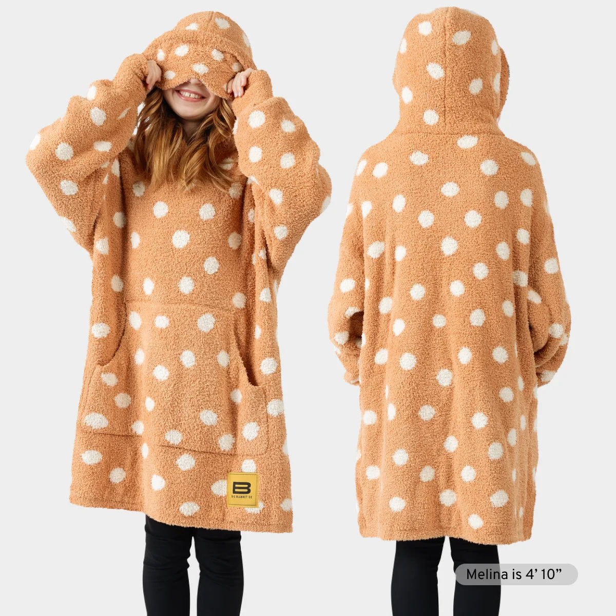 Tan oversized hoodie blanket with white polka dots, shown front and back on child model wearing black leggings