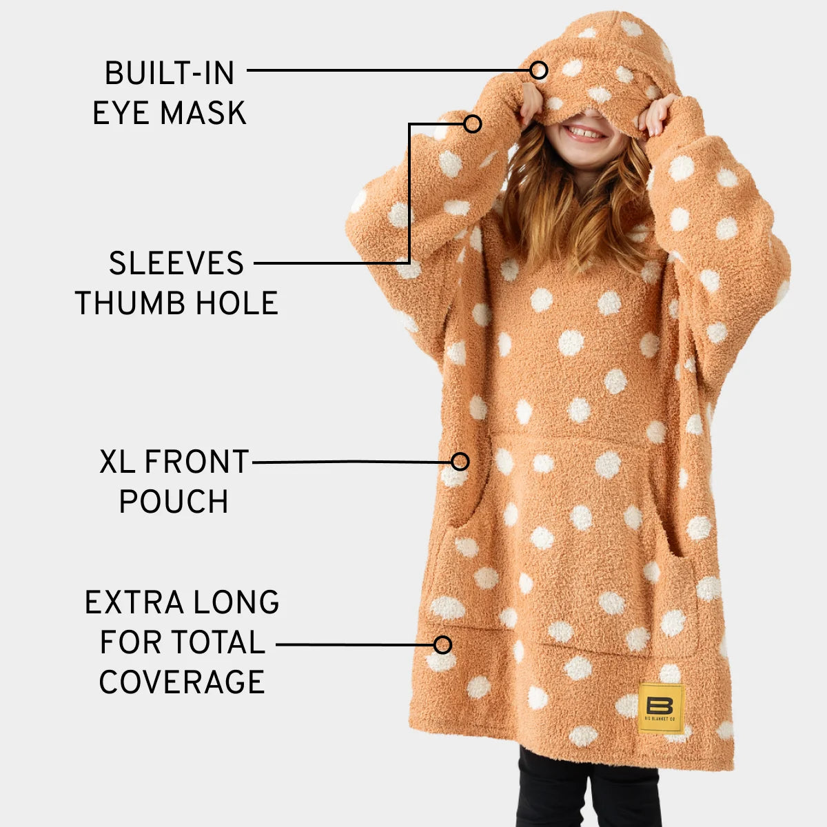 Child wearing tan Premier Plush Hoodie with white polka dots, featuring built-in eye mask, thumb holes, and oversized front pouch