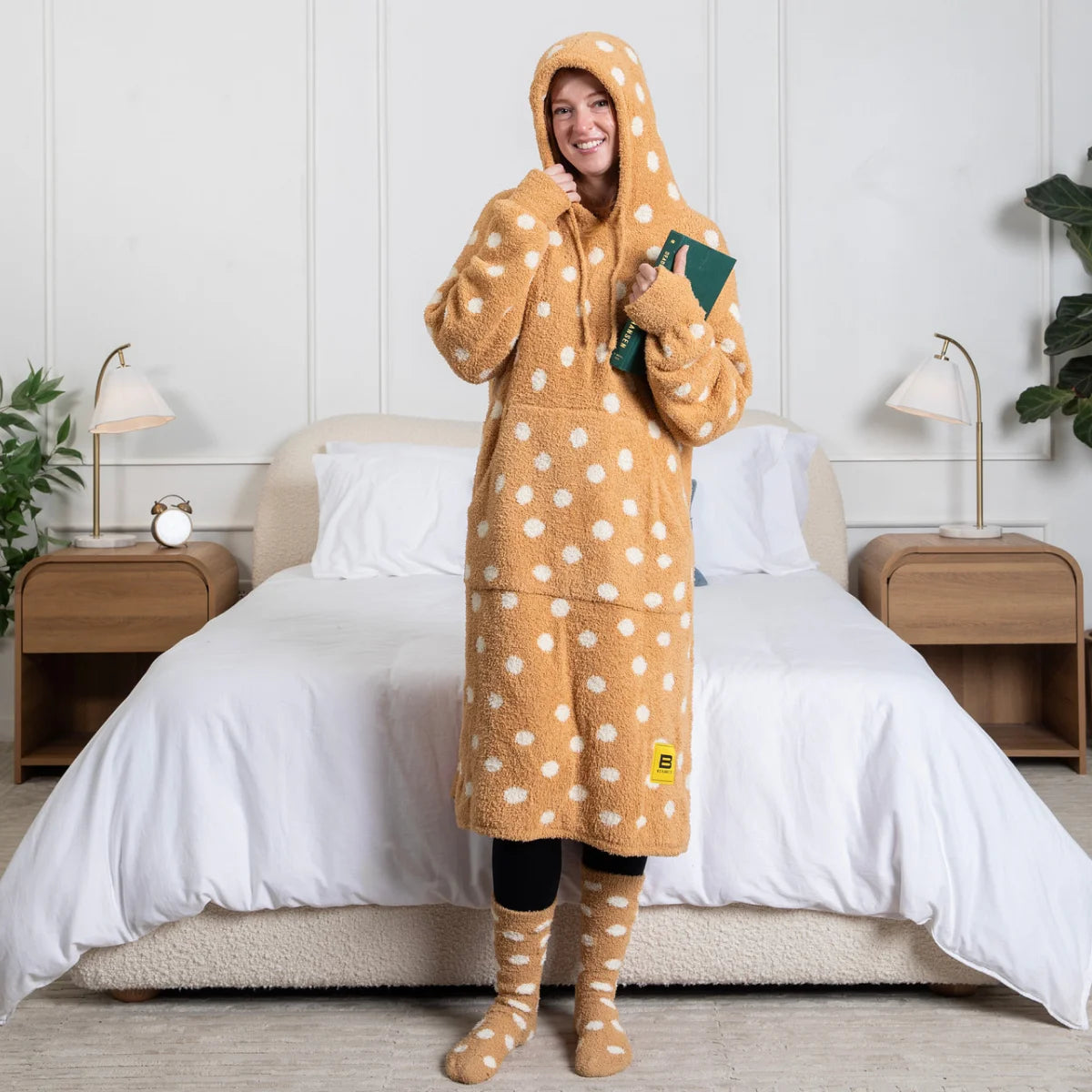 Child wrapped in tan oversized blanket hoodie with white polka dots, holding popcorn bowl on gray sofa