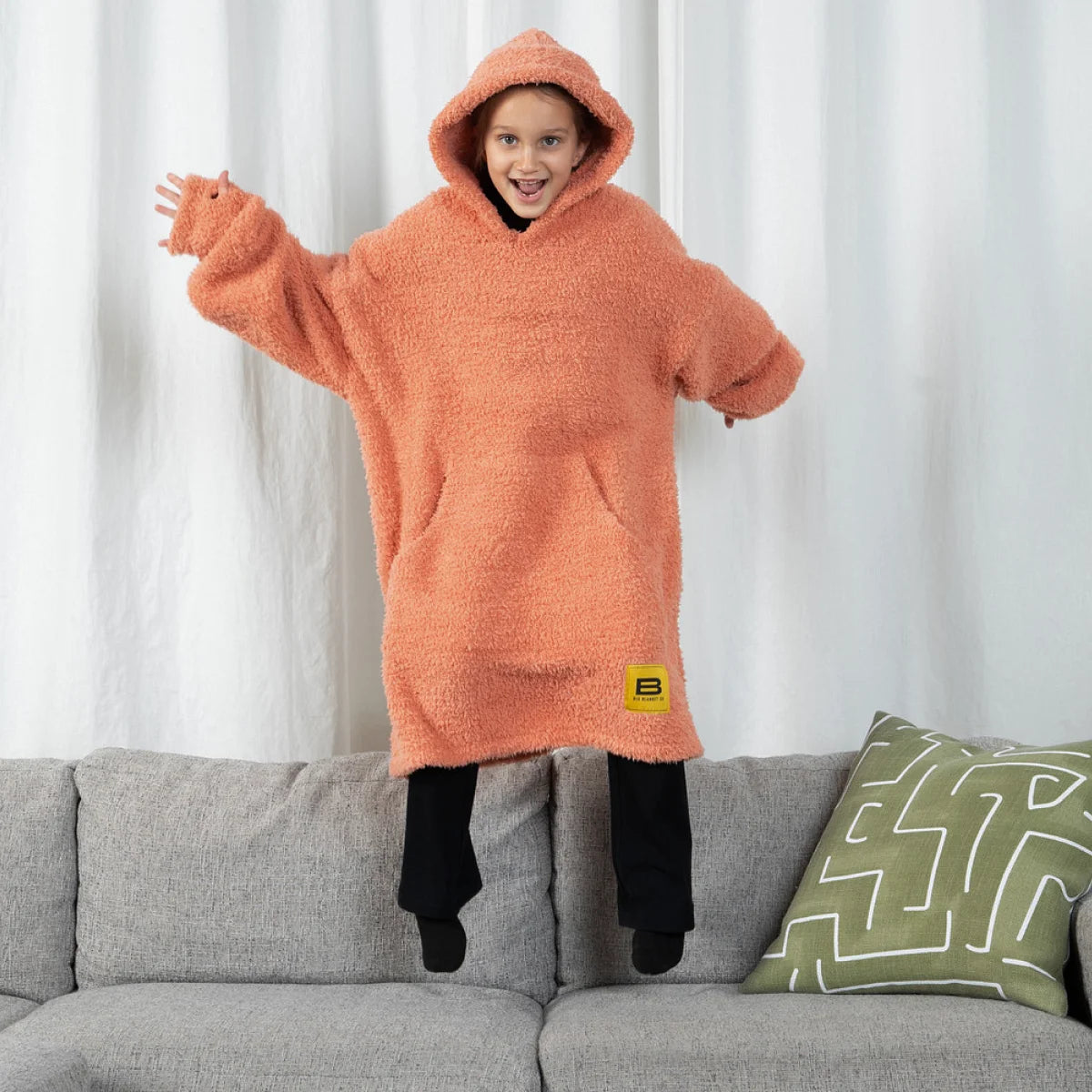 Person wrapped in oversized terracotta textured hoodie blanket on white bedding
