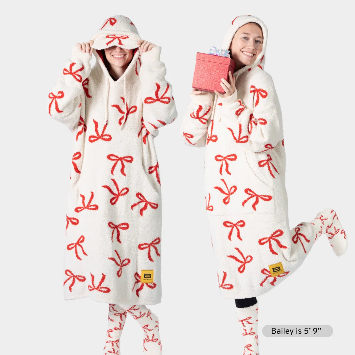Cream oversized hoodie blanket with red bow pattern, modeled by two people wearing matching coordinating pieces and holiday accessories