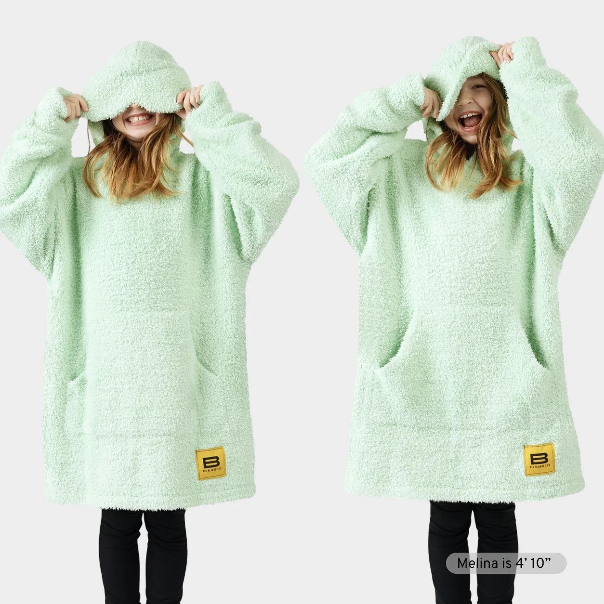 Child wearing mint green oversized hoodie blanket with front pocket and hood pulled over head, showing cozy fit and texture