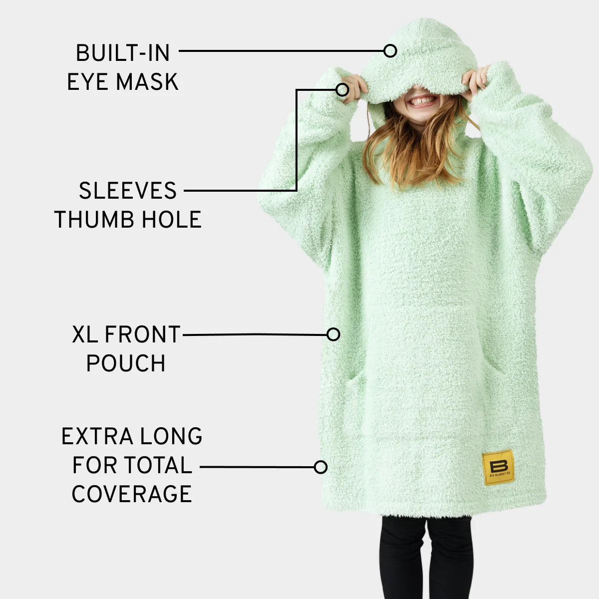 Mint green oversized hoodie blanket with built-in eye mask, sleeve thumb holes, and XL front pouch, shown on child