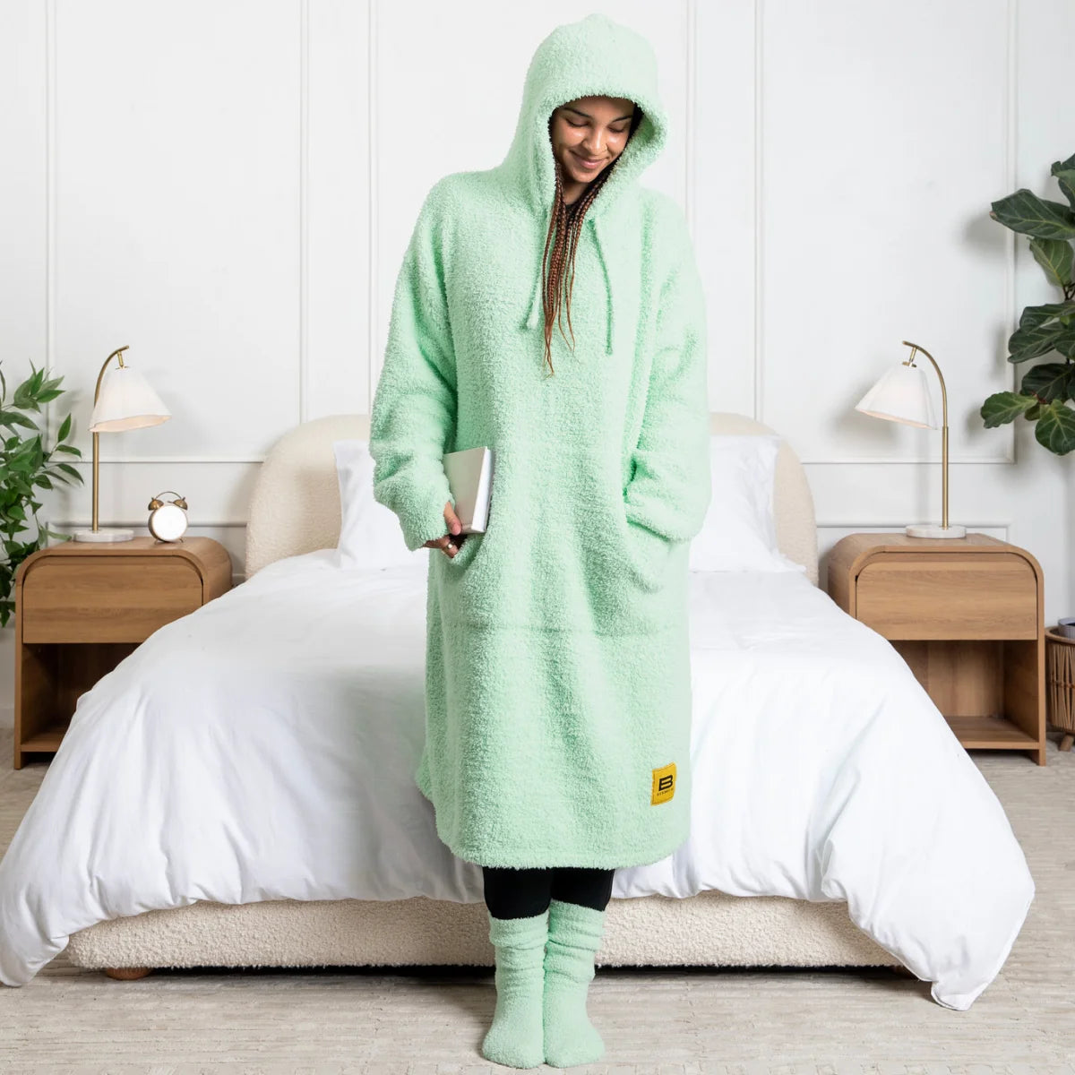 Child wrapped in mint green oversized hoodie blanket with hood up, holding gaming controller on gray couch