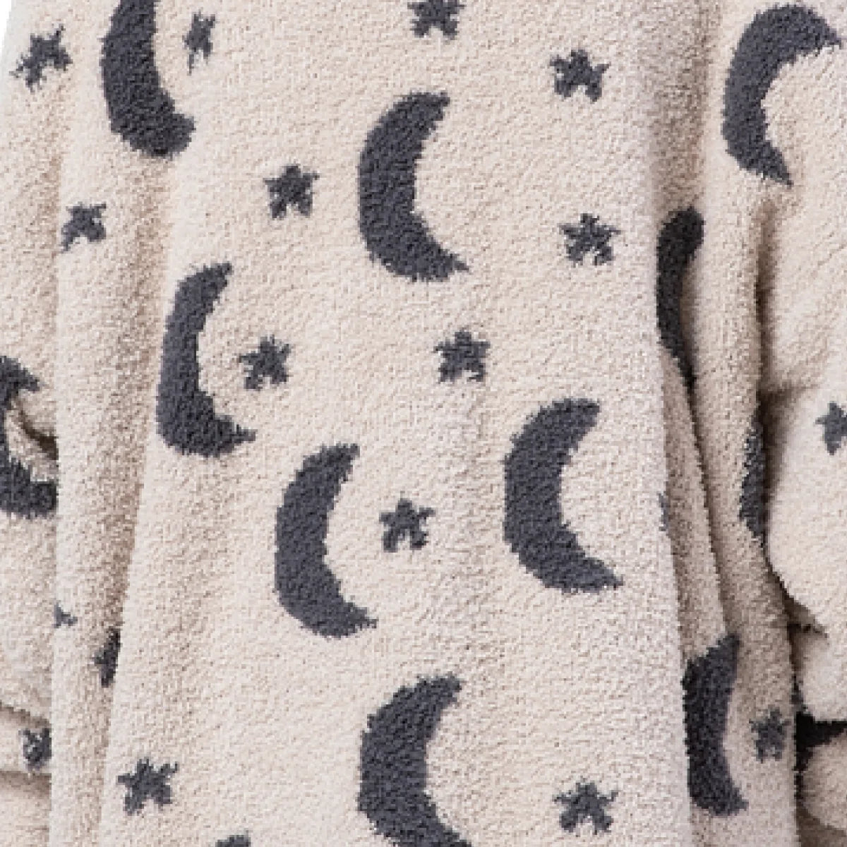 Cream oversized blanket with charcoal moons and stars pattern, draped showing soft plush texture