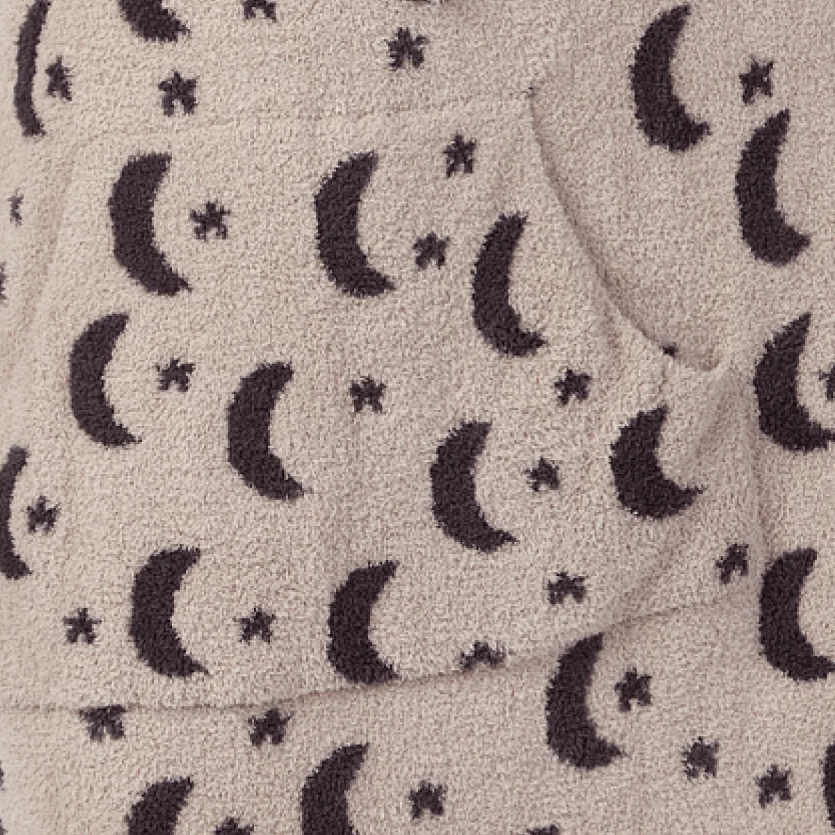 Child wearing cream Premier Plush Hoodie with navy moon and star pattern, hood covering head, holding stuffed bear on brown sofa