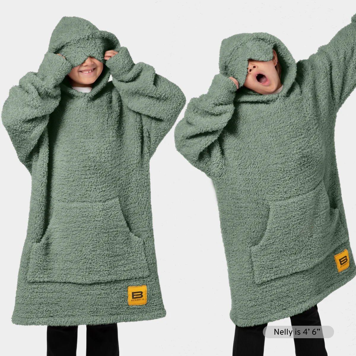 Sage green oversized hoodie blanket with kangaroo pouch and drawstring hood, shown on two models wearing matching socks