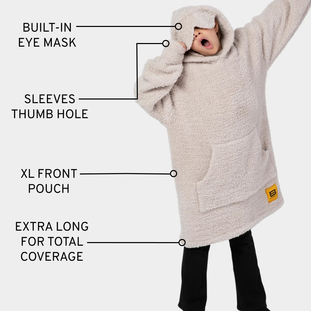 Woman wearing oatmeal oversized hoodie blanket with eye mask, thumb holes, and front pouch, featuring extra-long coverage