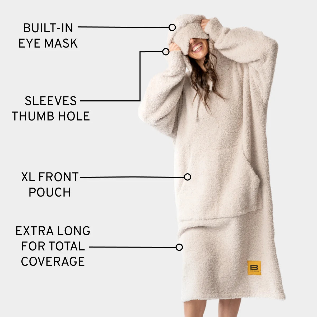 Woman wearing cream oversized blanket hoodie with built-in eye mask, thumb holes, and front pouch, featuring extra-long coverage
