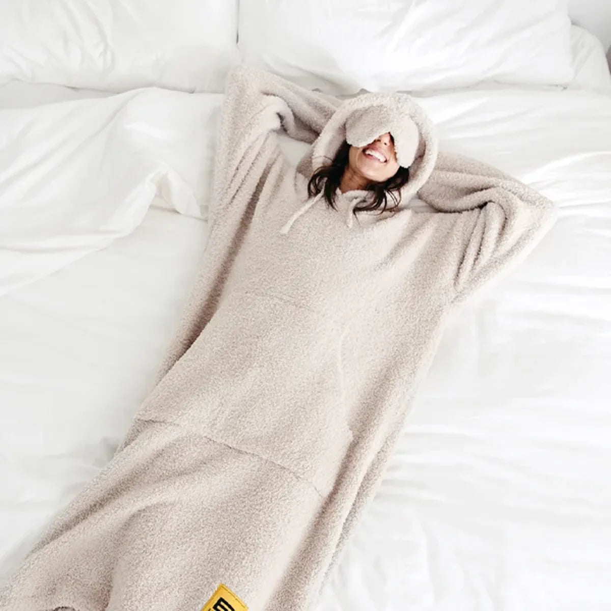 Child wrapped in oversized beige hoodie blanket on white bedding, peeking out from cozy fabric
