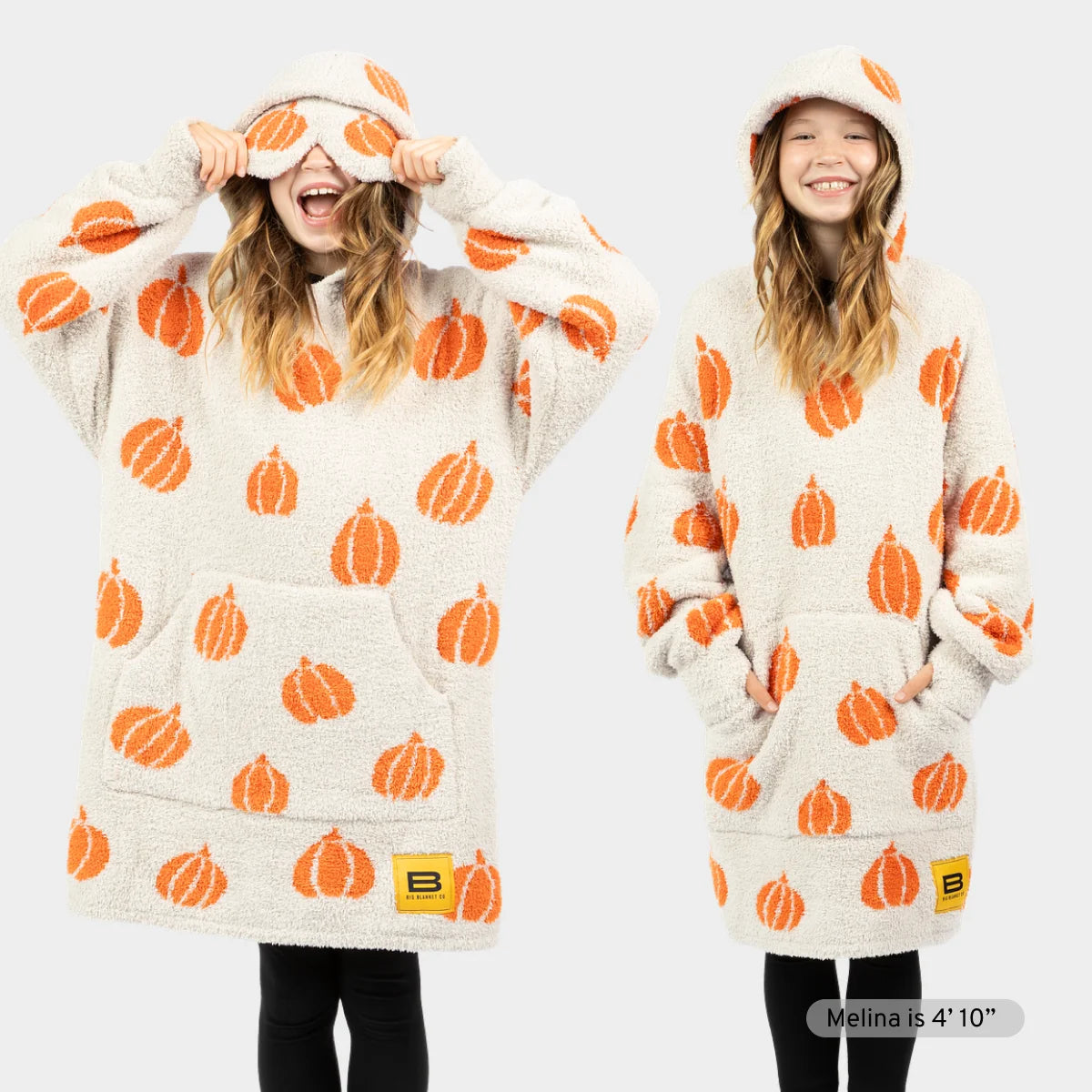 Cream oversized hoodie blanket with orange pumpkin pattern, worn by two women showing hood and full-length coverage