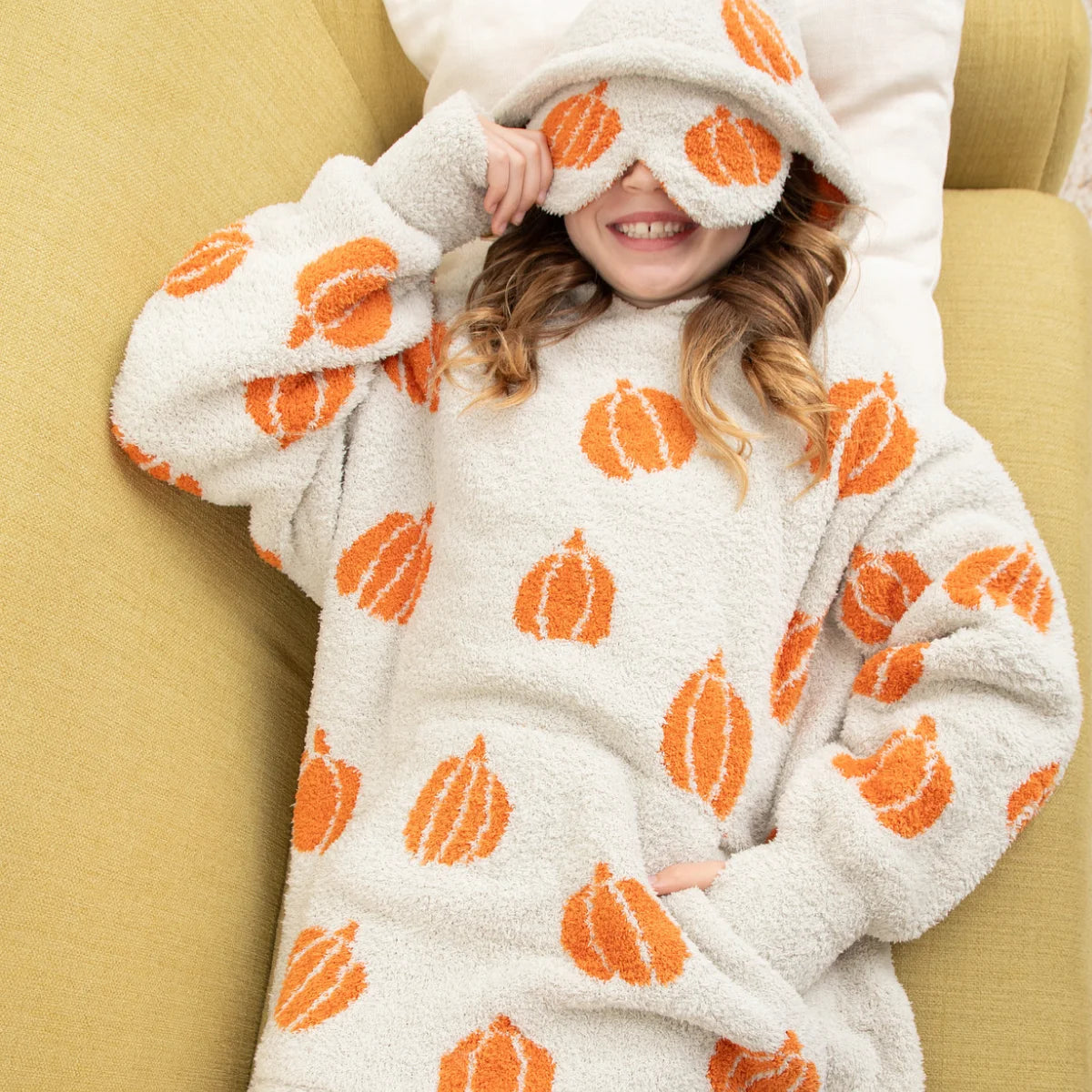Cream oversized hoodie blanket with orange pumpkin pattern, worn by smiling child on bed with hood covering eyes