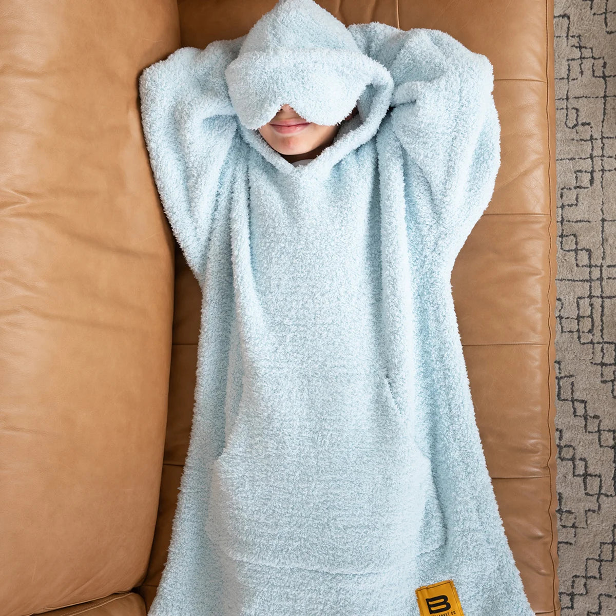 Child wrapped in sky blue oversized hoodie blanket on white bed, peeking out from cozy fabric