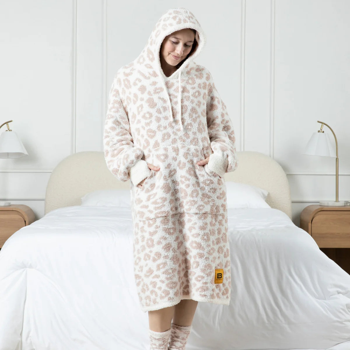 Woman wearing cream and taupe leopard print oversized hoodie blanket with hood and kangaroo pockets on bed