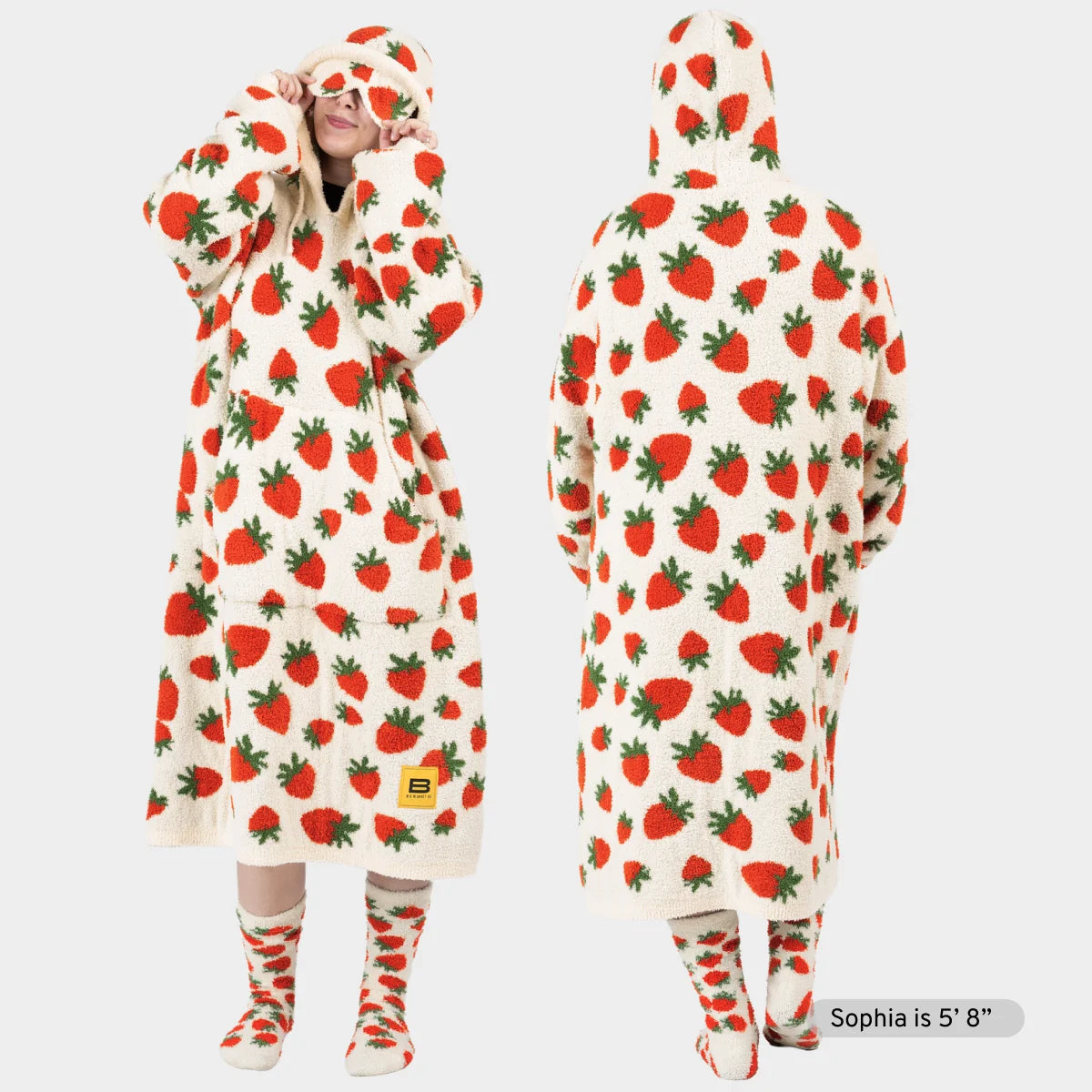 Cream oversized hoodie blanket with red strawberry and green leaf pattern, shown front and back on model wearing matching socks