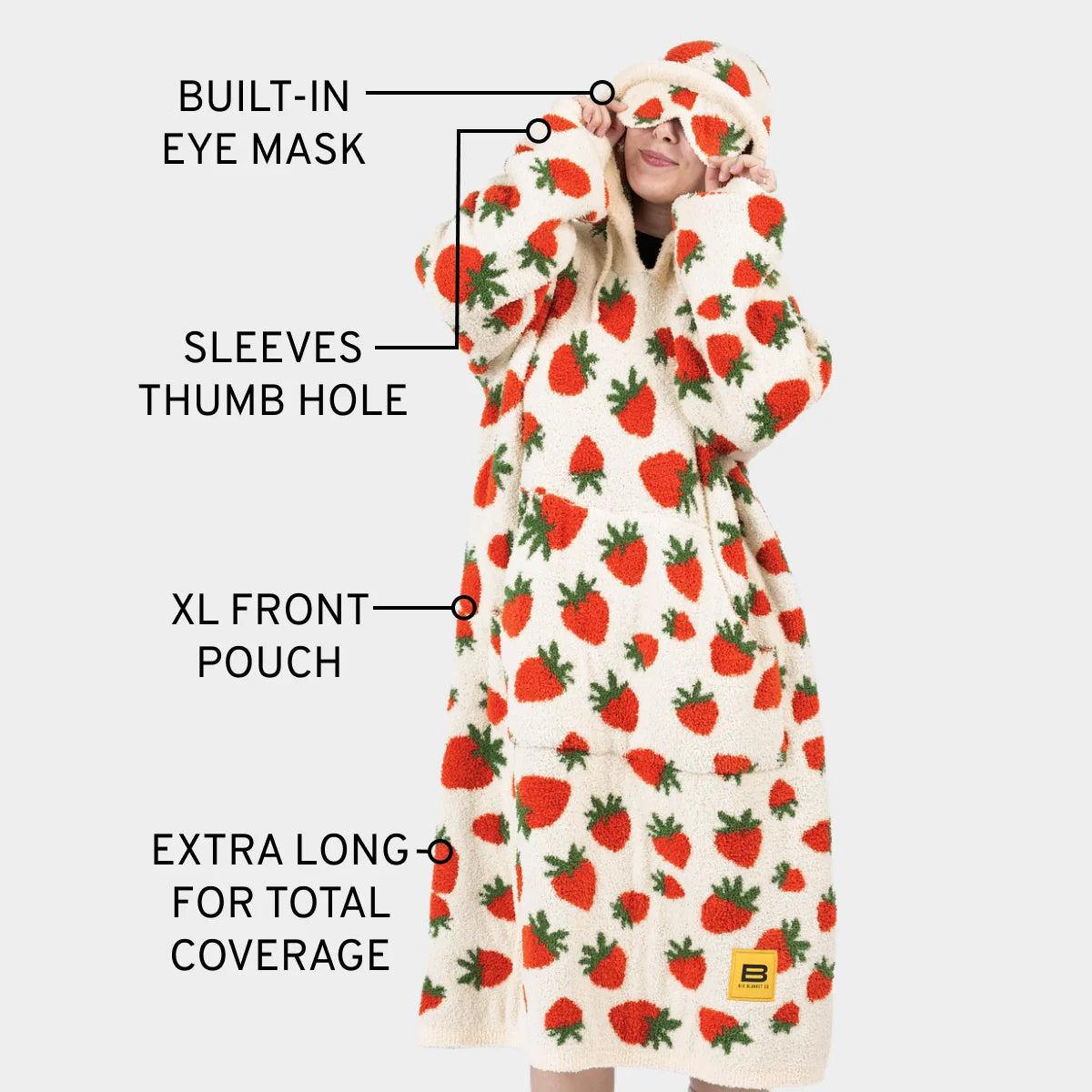 Cream oversized blanket hoodie with red strawberry print, featuring built-in eye mask, sleeves with thumb holes, XL front pouch, and extra-long coverage