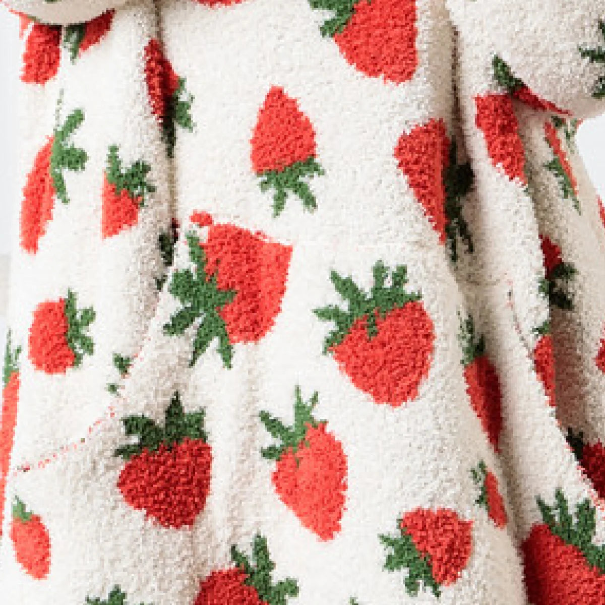 Cream oversized blanket with red strawberry and green leaf pattern, draped to show texture and scale