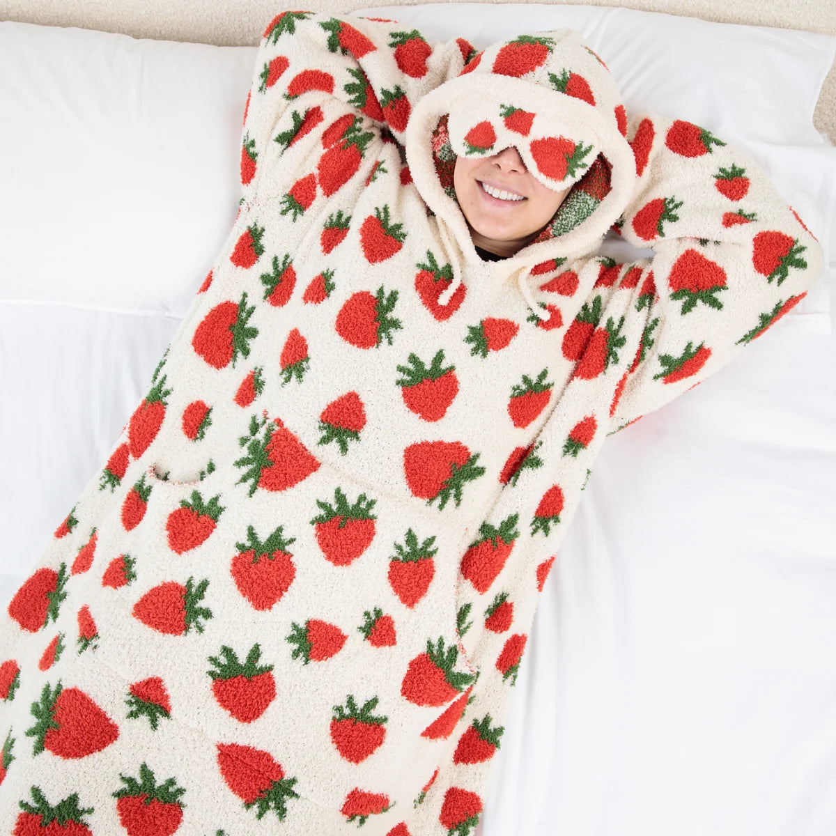 Person wrapped in cream oversized blanket with red strawberry and green leaf pattern, hood pulled up