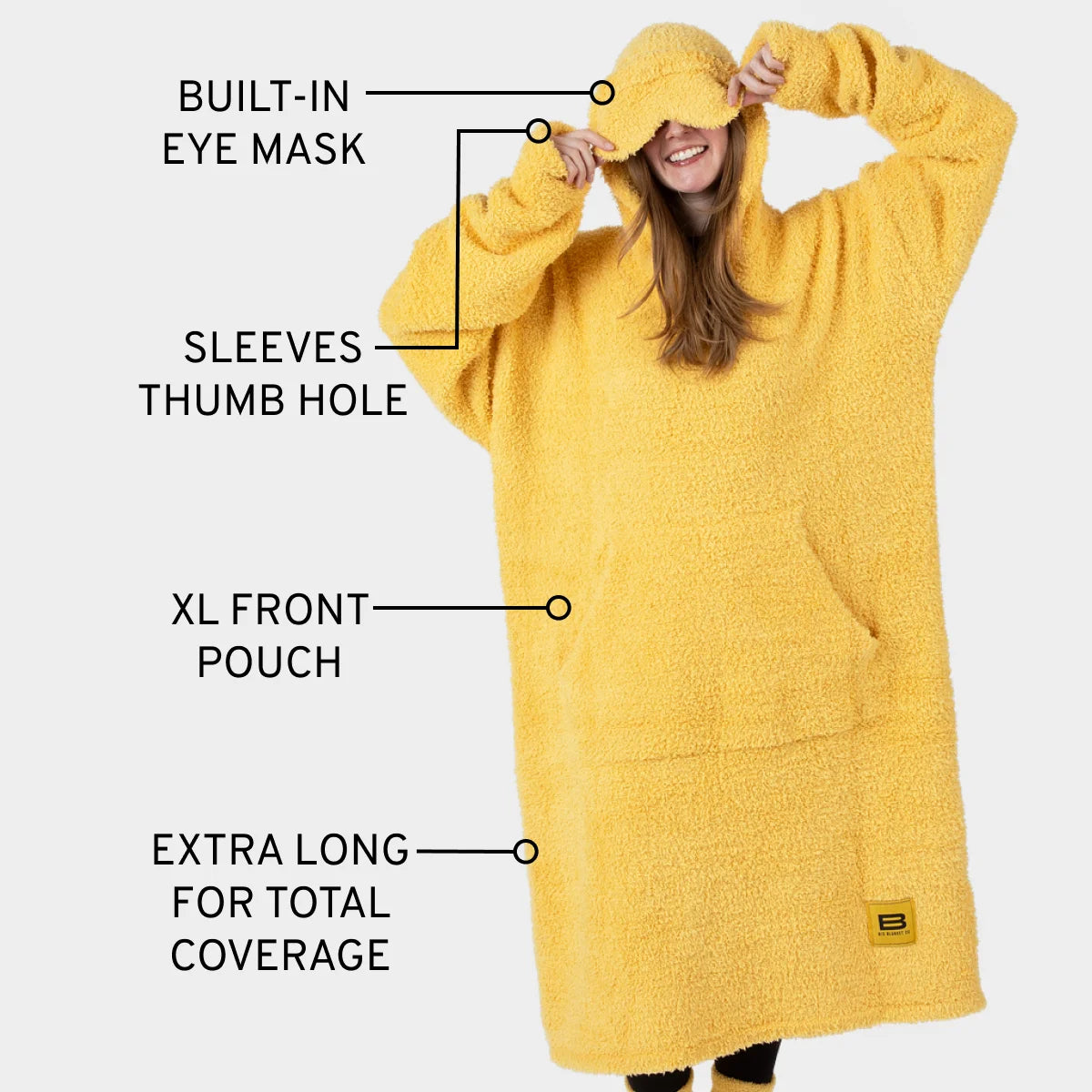 Woman wearing yellow Premier Plush Hoodie with built-in eye mask, thumb hole sleeves, XL front pouch, and extra-long coverage