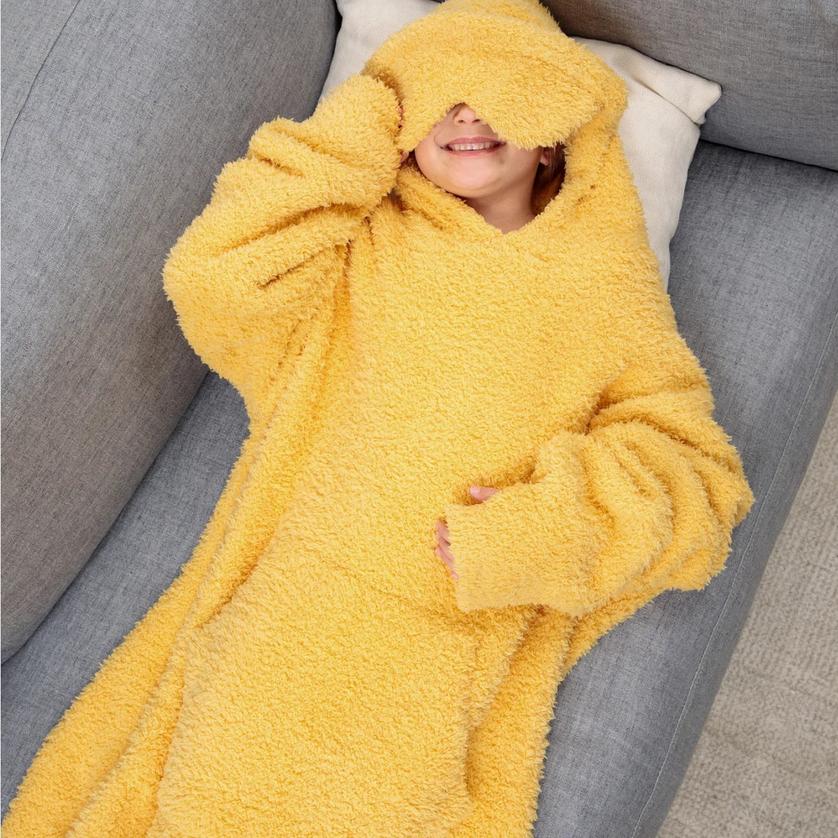 Woman wearing oversized sunflower yellow hoodie blanket while reading on bed