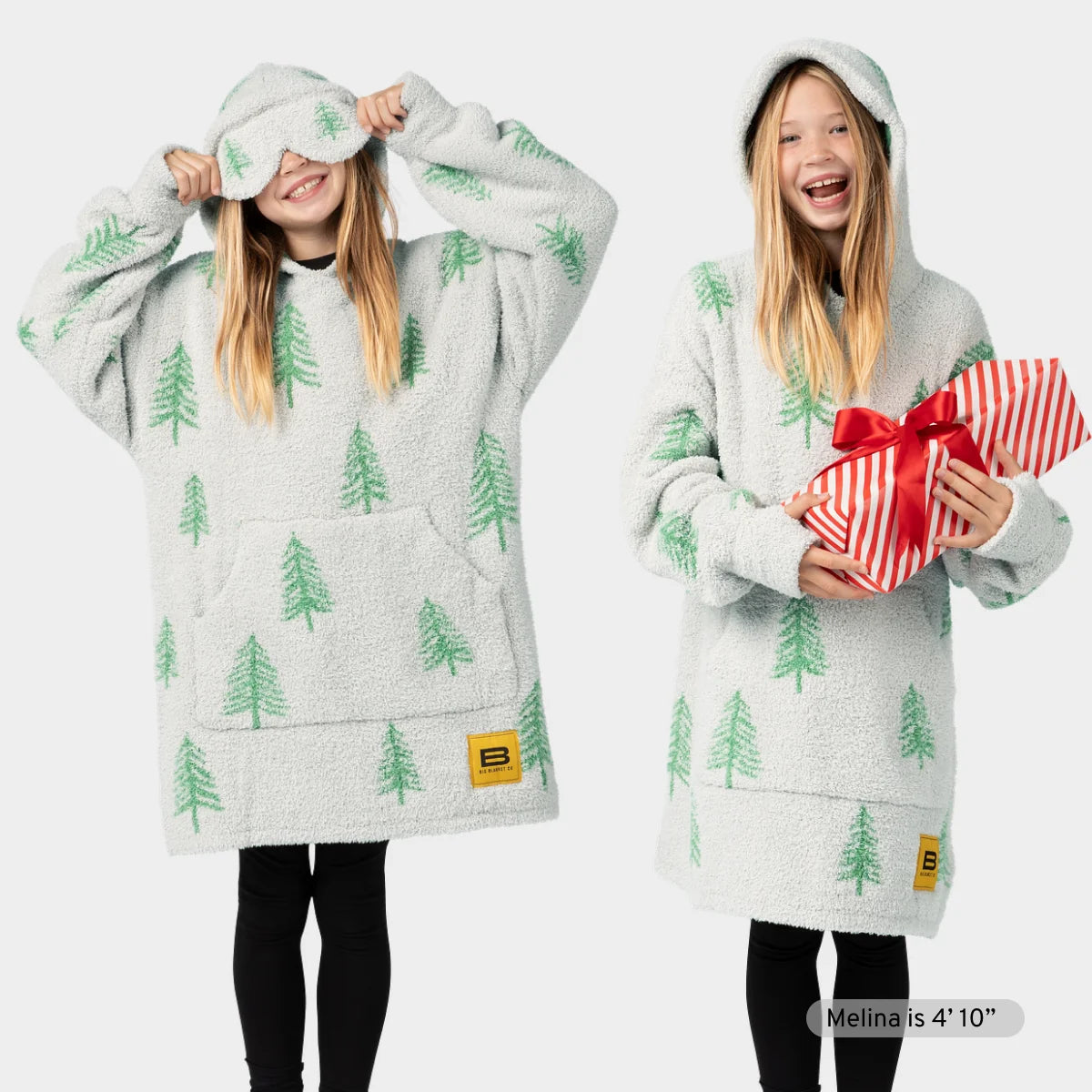Cream oversized hoodie blanket with green pine tree pattern, shown on two people wearing the garment with hood up