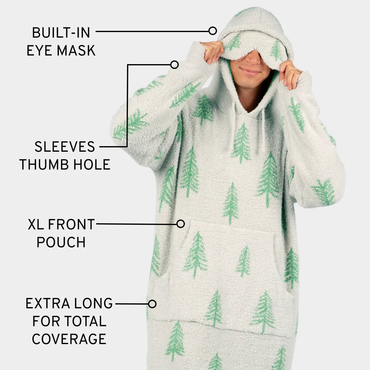 Cream oversized hoodie blanket with green pine tree pattern, built-in eye mask, thumb hole sleeves, and extra-long length for total coverage