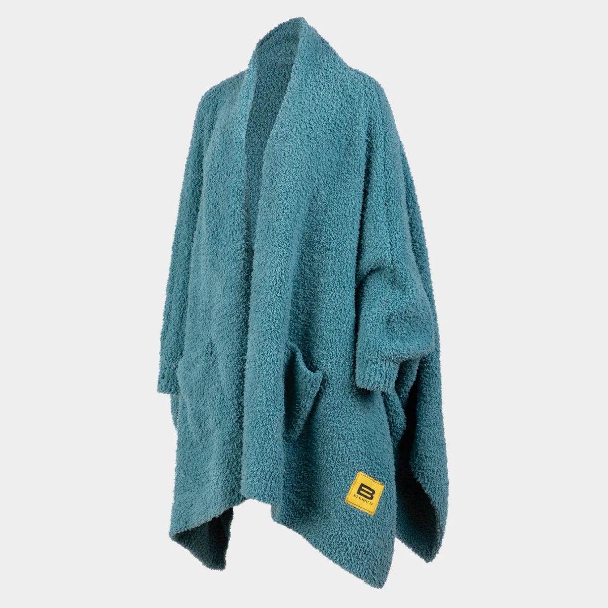 Teal oversized blanket wrap with soft textured fabric, yellow brand label, draped on form against white background