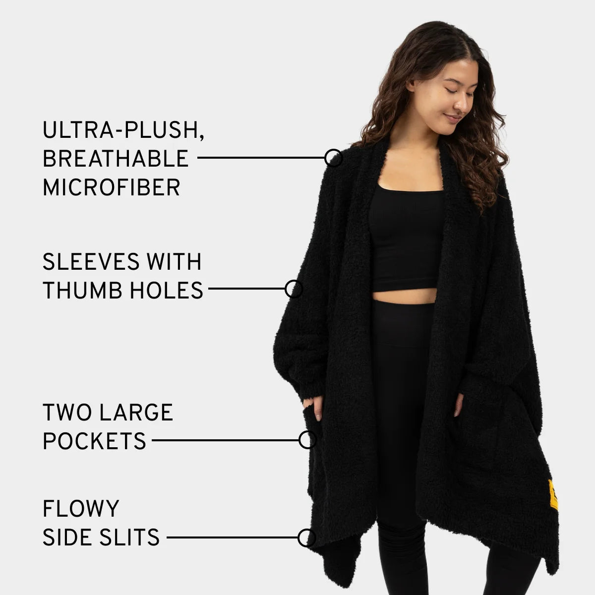 Black oversized blanket wrap with thumb holes, pockets, and side slits, modeled by woman showing ultra-plush microfiber fabric