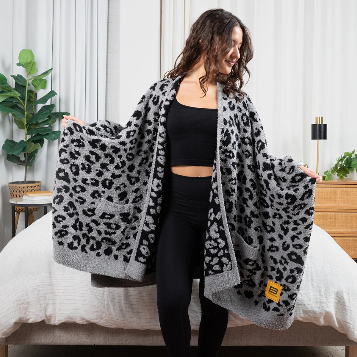 Woman wearing gray and black leopard print oversized blanket draped over shoulders on bed