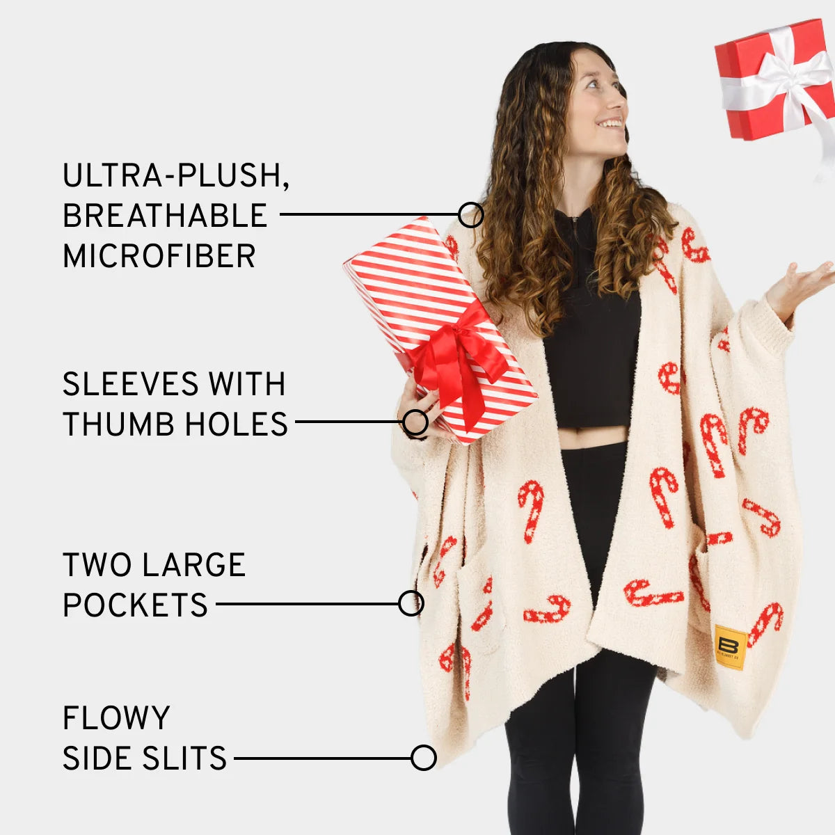 Woman wearing cream oversized blanket wrap with red candy cane pattern, thumb hole sleeves, pockets, and side slits
