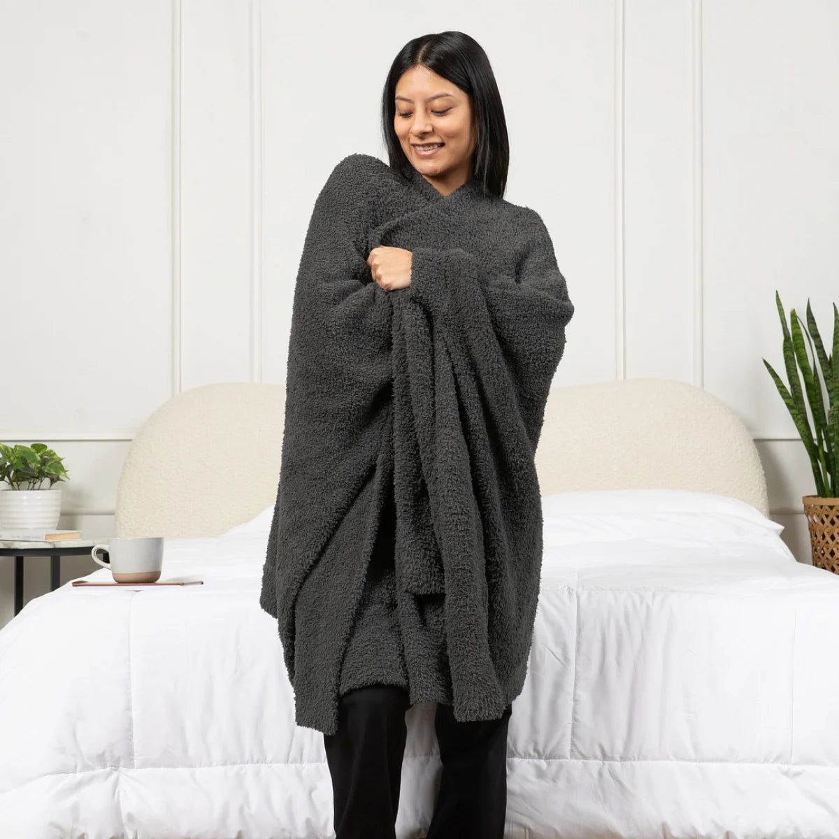 Woman wrapped in charcoal gray oversized blanket on bed, showing plush texture and generous coverage